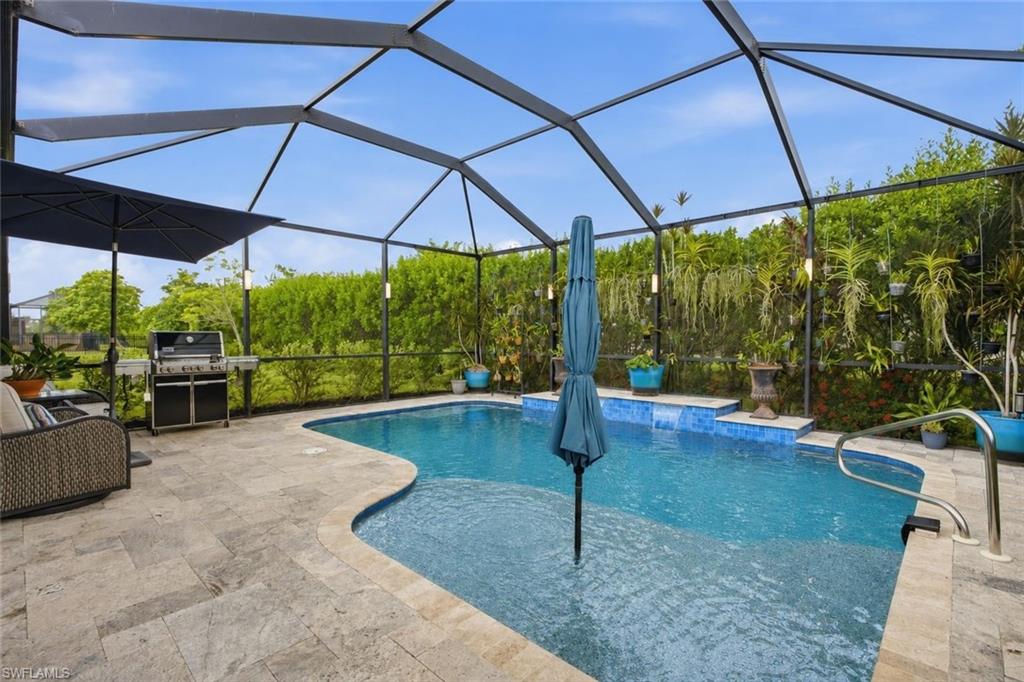 Screen-enclosed outdoor living area featuring a freeform swimming pool, integrated water feature, and extensive paver decking
