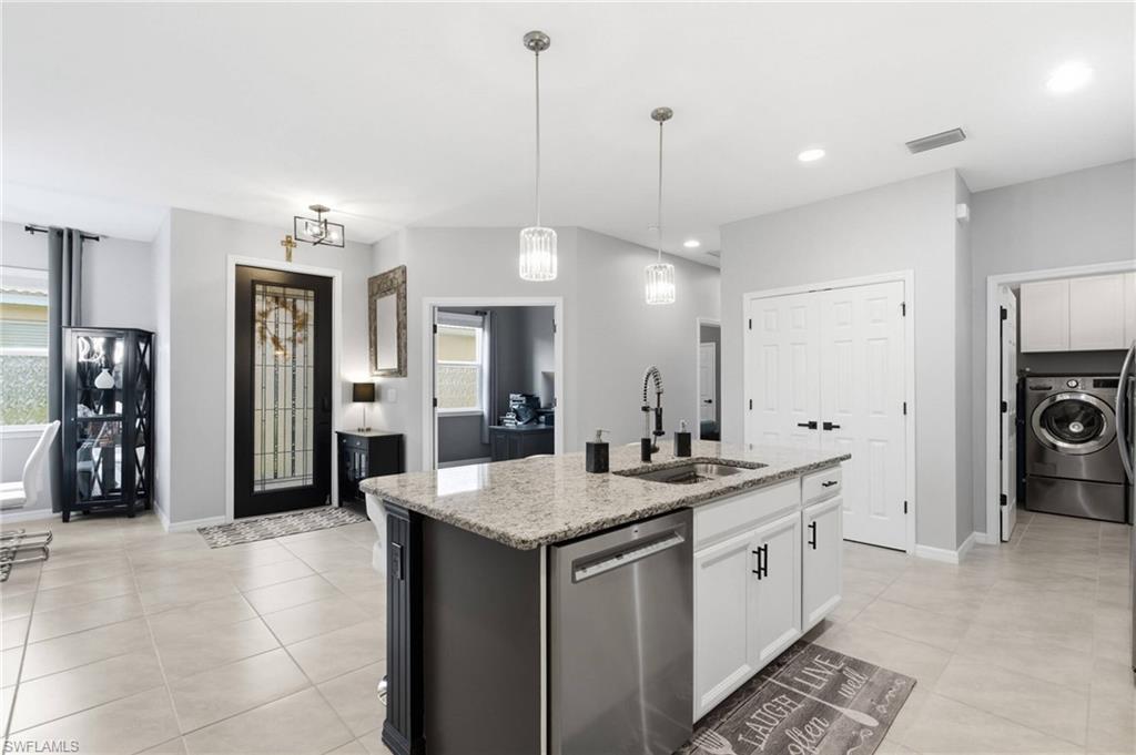 Open-concept kitchen featuring a central island with a granite countertop, built-in sink, and stainless steel dishwasher