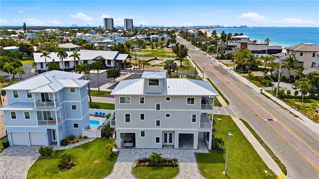 Coastal property featuring multiple balconies, a metal roof, and a paver driveway - Virtually Edited Image