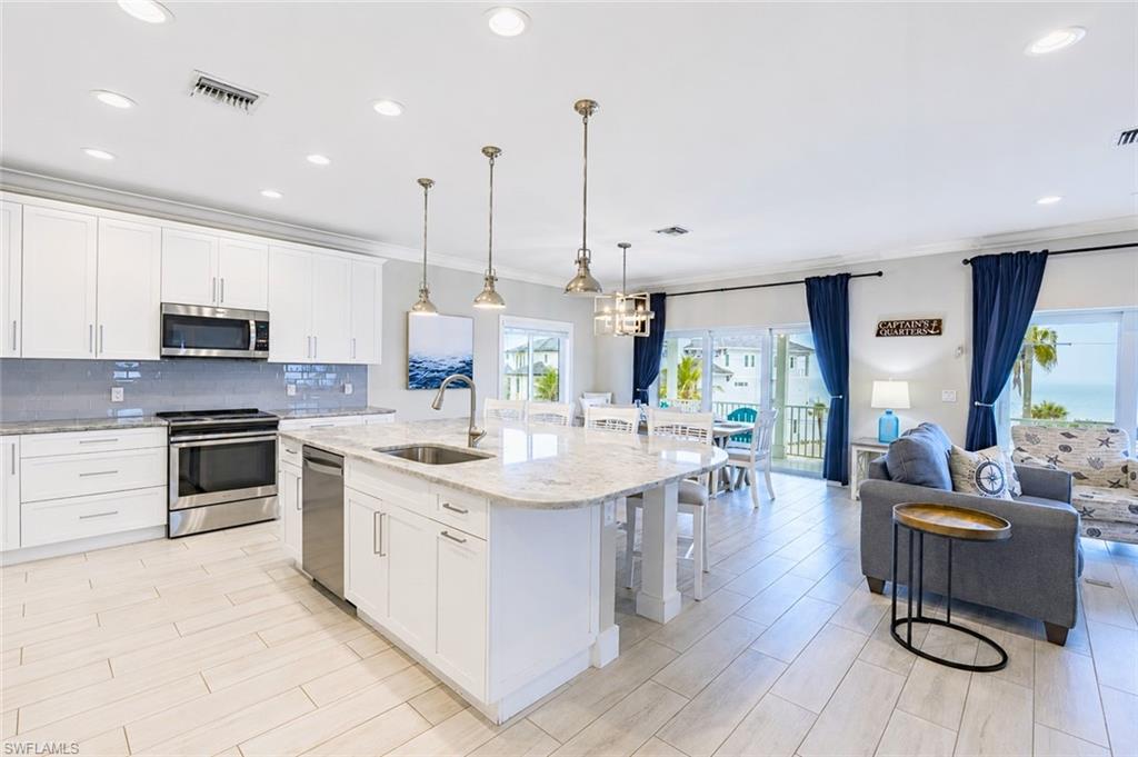 Open-concept living area featuring a modern kitchen with white cabinetry, stainless steel appliances, and a large island with an integrated sink - Virtually Edited Image