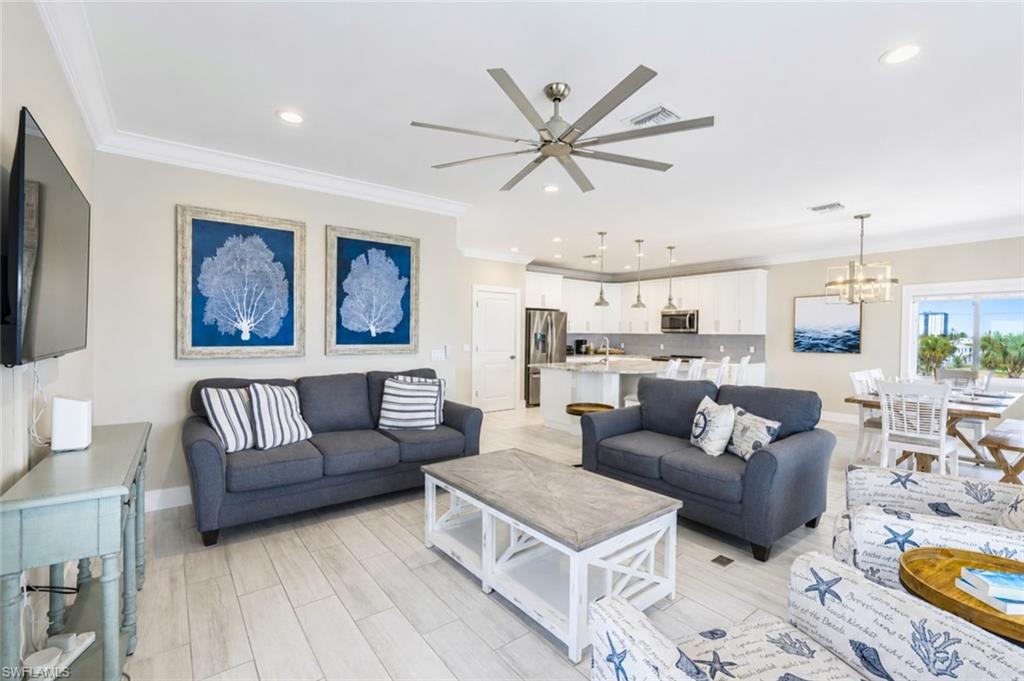 Open-concept living area featuring light wood-finish flooring, recessed lighting, and a large ceiling fan - Virtually Edited Image