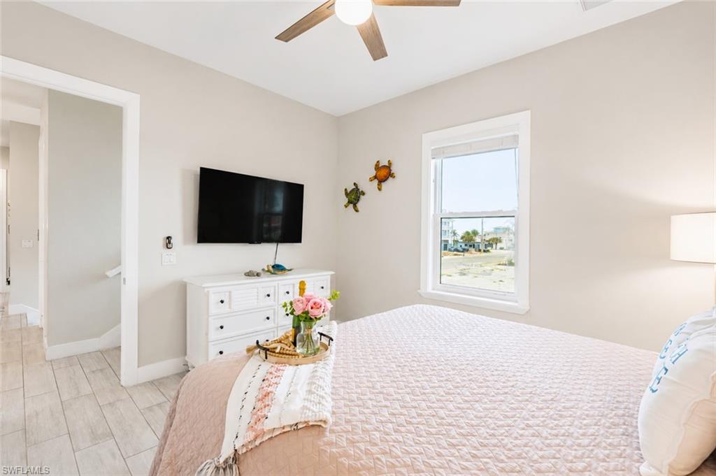 Bedroom featuring wood-finish flooring, a ceiling fan, and a window with white trim - Virtually Edited Image