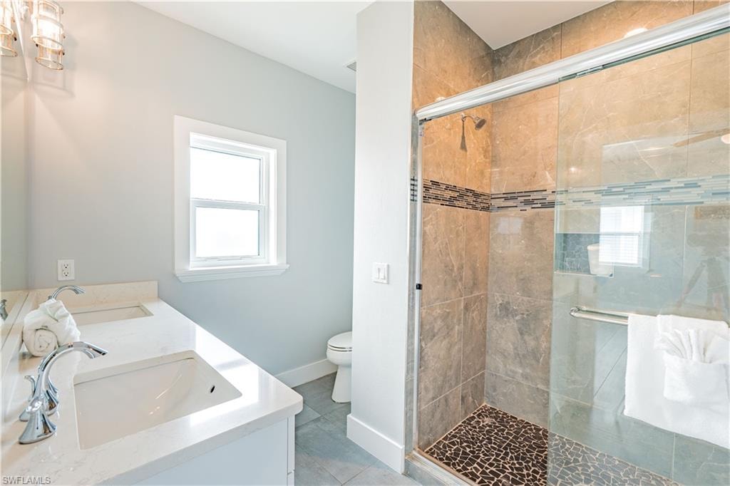 Bathroom featuring a double vanity with integrated sinks, a walk-in shower with a glass enclosure, and stone-look wall and floor tiling - Virtually Edited Image