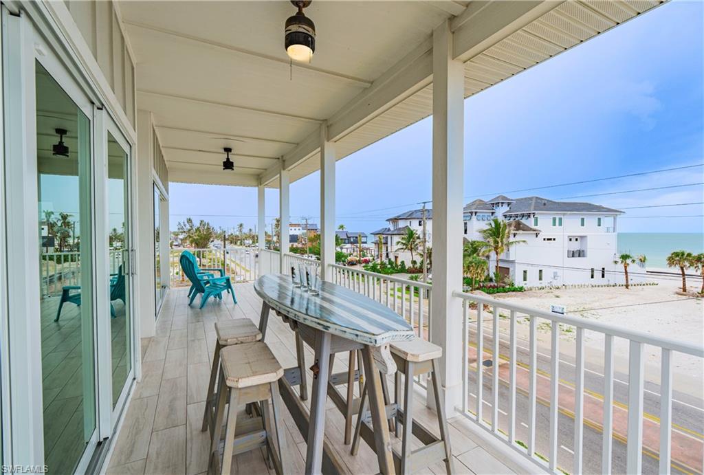 Expansive covered balcony featuring wood-finish flooring, white railing, and multiple ceiling-mounted light fixtures - Virtually Edited Image