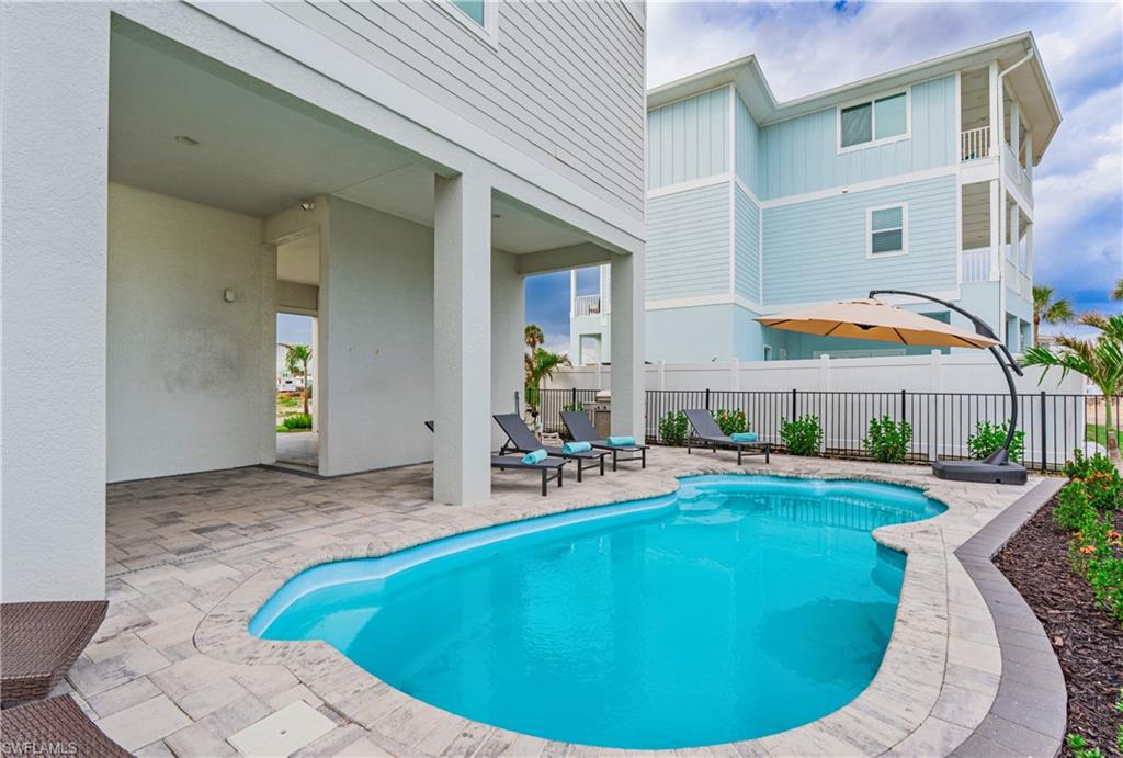 Private outdoor living area featuring a custom-shaped swimming pool, paver patio, covered porch area, and perimeter fencing - Virtually Edited Image