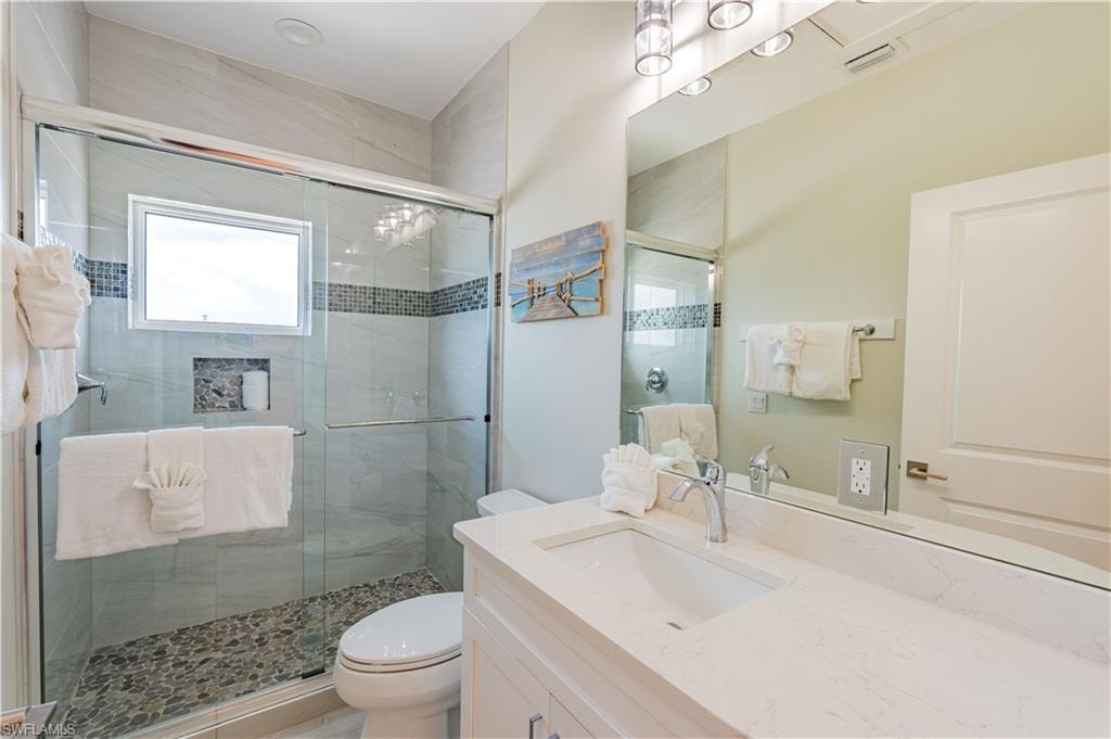 Bathroom featuring a shower with glass enclosure, pebble-finish flooring, a built-in shelf, and a horizontal window - Virtually Edited Image