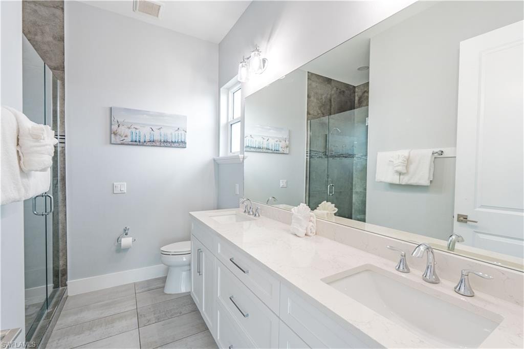 Bathroom featuring a dual vanity with integrated sinks, a glass-enclosed shower, a large wall-mounted mirror, light gray wall paint, and wood-finish tile flooring - Virtually Edited Image