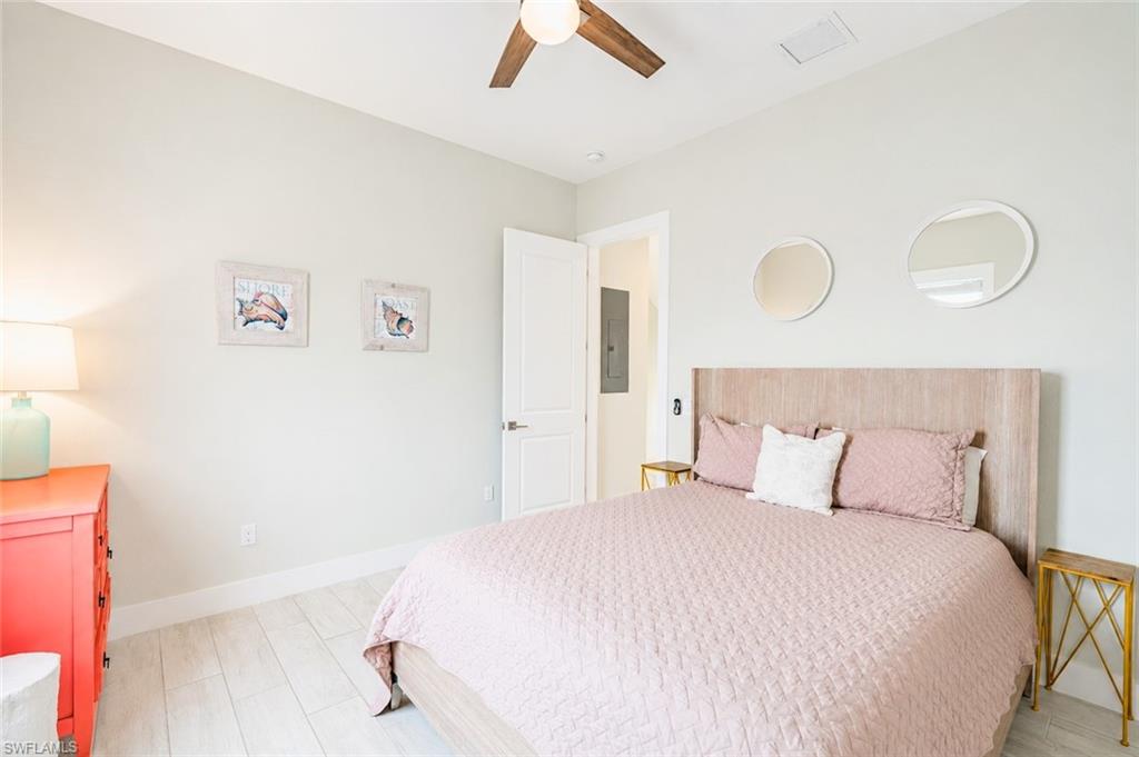 Bright bedroom featuring wood-finish flooring, a contemporary ceiling fan, and a light-toned wood headboard - Virtually Edited Image