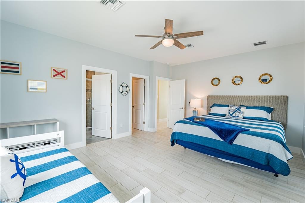 Spacious room featuring light wood-finish flooring, a ceiling fan with integrated lighting, and multiple white panel doors - Virtually Edited Image