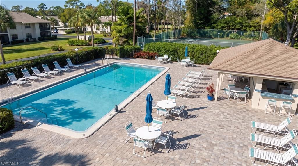 Resort-style pool area featuring a rectangular swimming pool, extensive paver decking, and a poolside cabana with a bar area