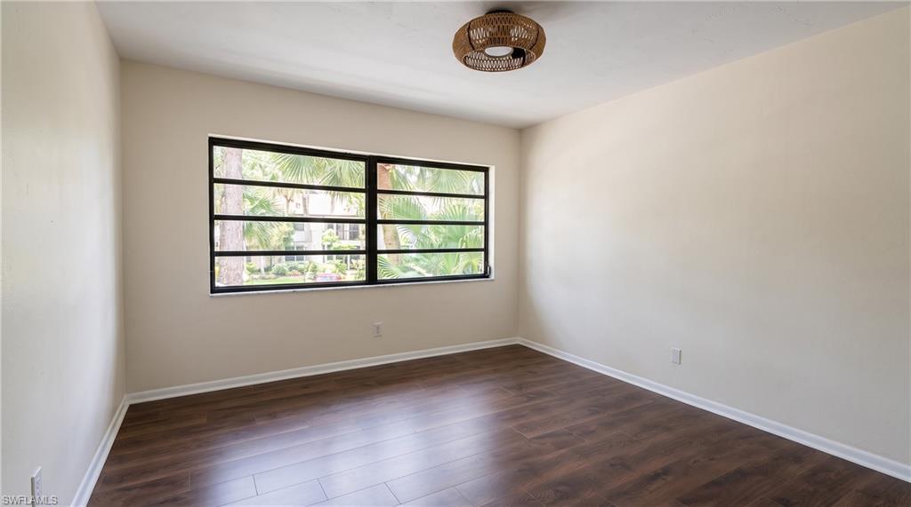 Spacious room featuring wood-finish flooring, neutral-toned walls, and a multi-pane window with black framing