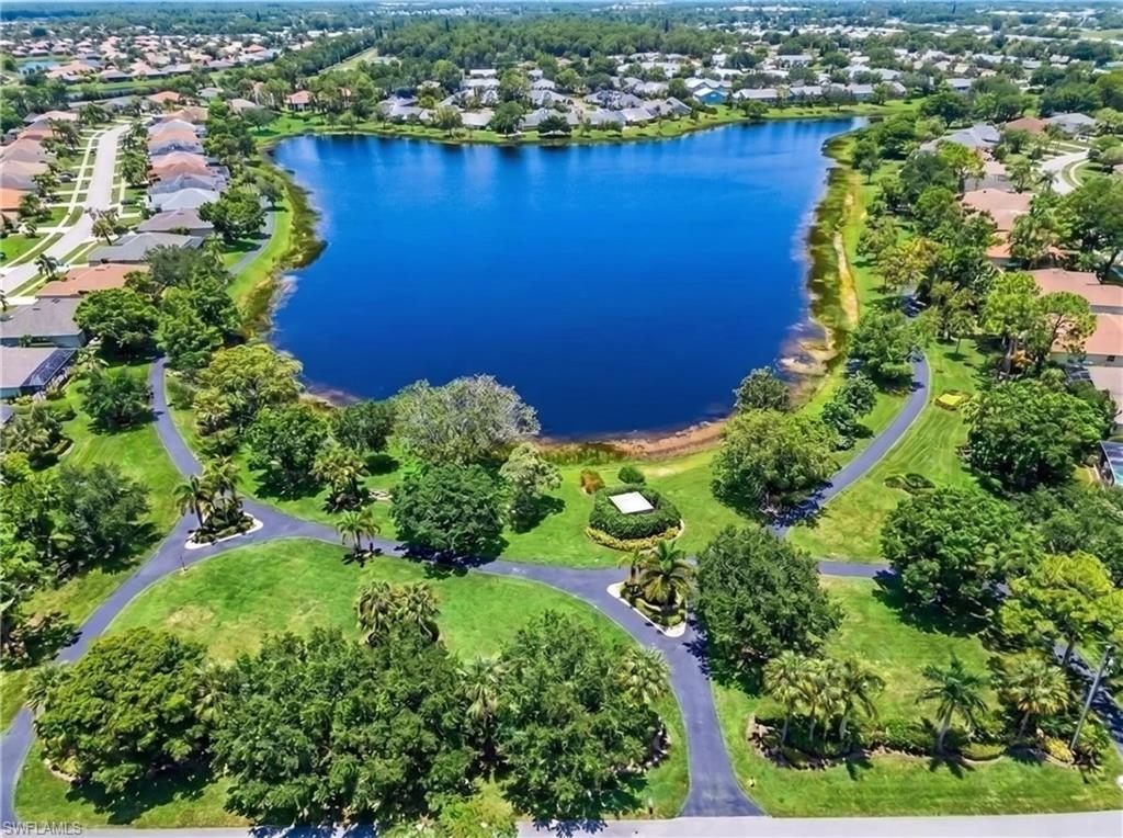 Expansive community lake surrounded by mature trees, manicured green spaces, and paved walking paths