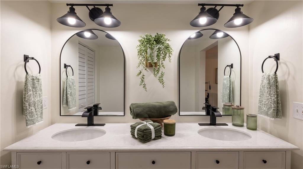 Dual vanity featuring individual vessel sinks, matte black faucets, arched mirrors, and coordinating overhead lighting