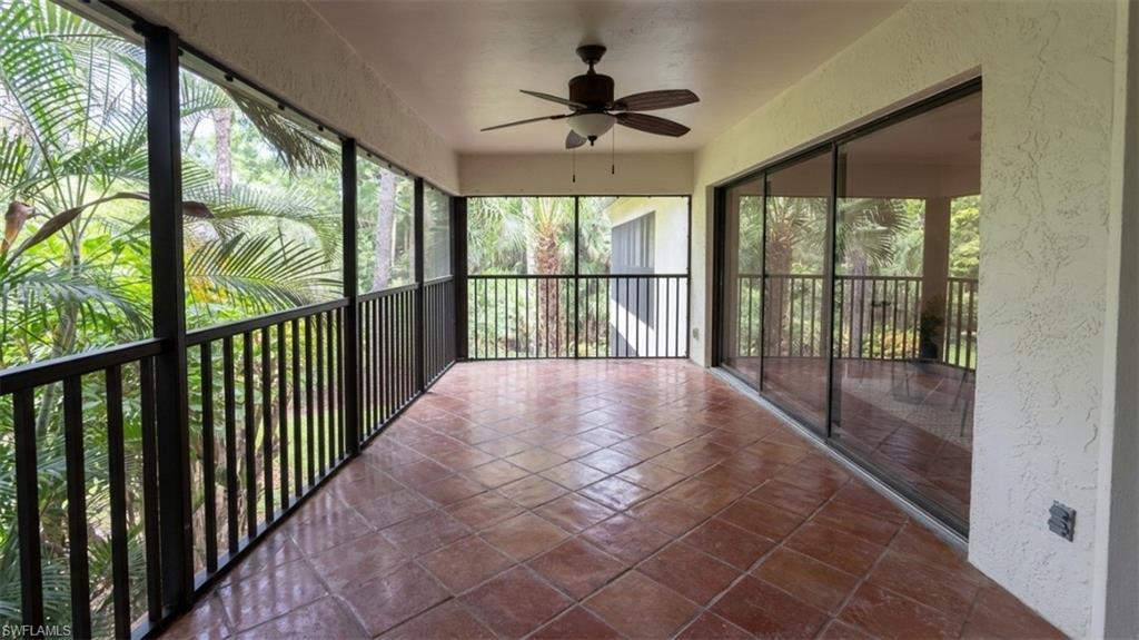 Spacious screened porch featuring terracotta-style tile flooring, a ceiling fan, and black railing