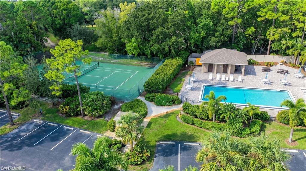 Outdoor recreational amenities featuring a fenced tennis court, a rectangular swimming pool, and a poolside building with a covered patio