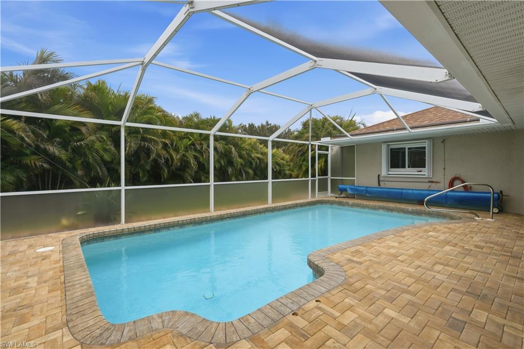 Screened enclosure encompassing a rectangular pool with curved entry, surrounded by a herringbone-pattern paver deck