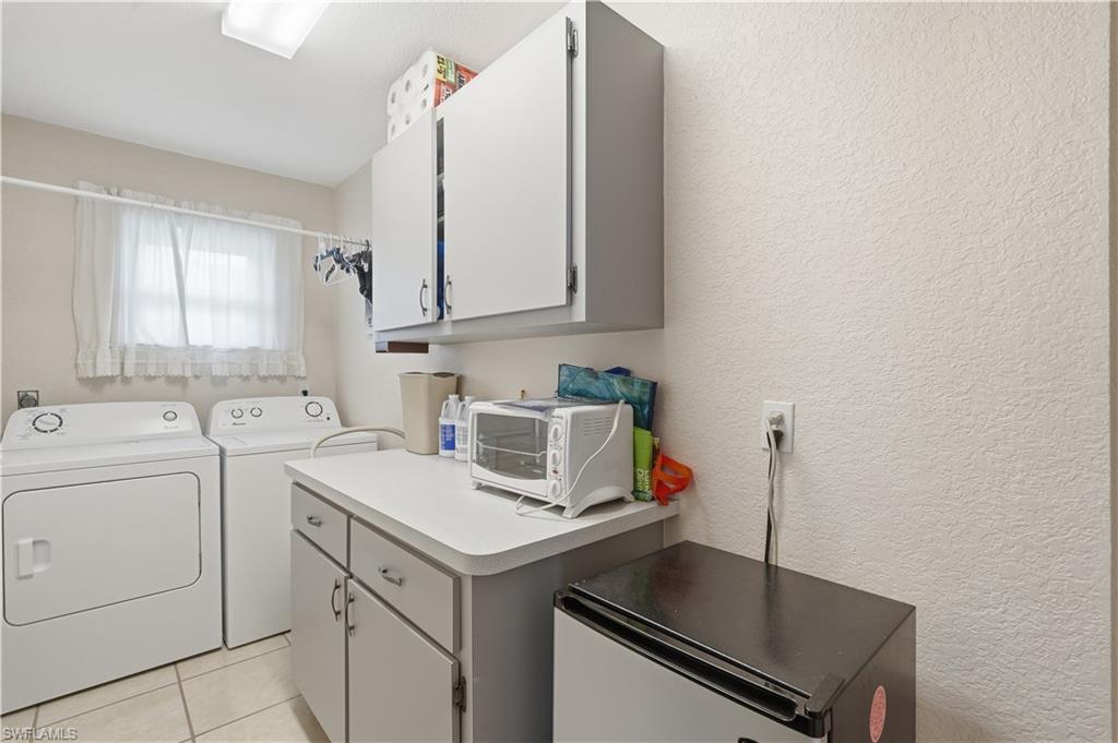 Dedicated laundry space featuring a window, built-in cabinetry, a countertop, an overhead light fixture, and tile flooring