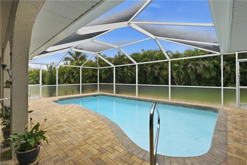 Screened-in pool area featuring a freeform pool with a handrail, paver decking, and a privacy screen along the perimeter