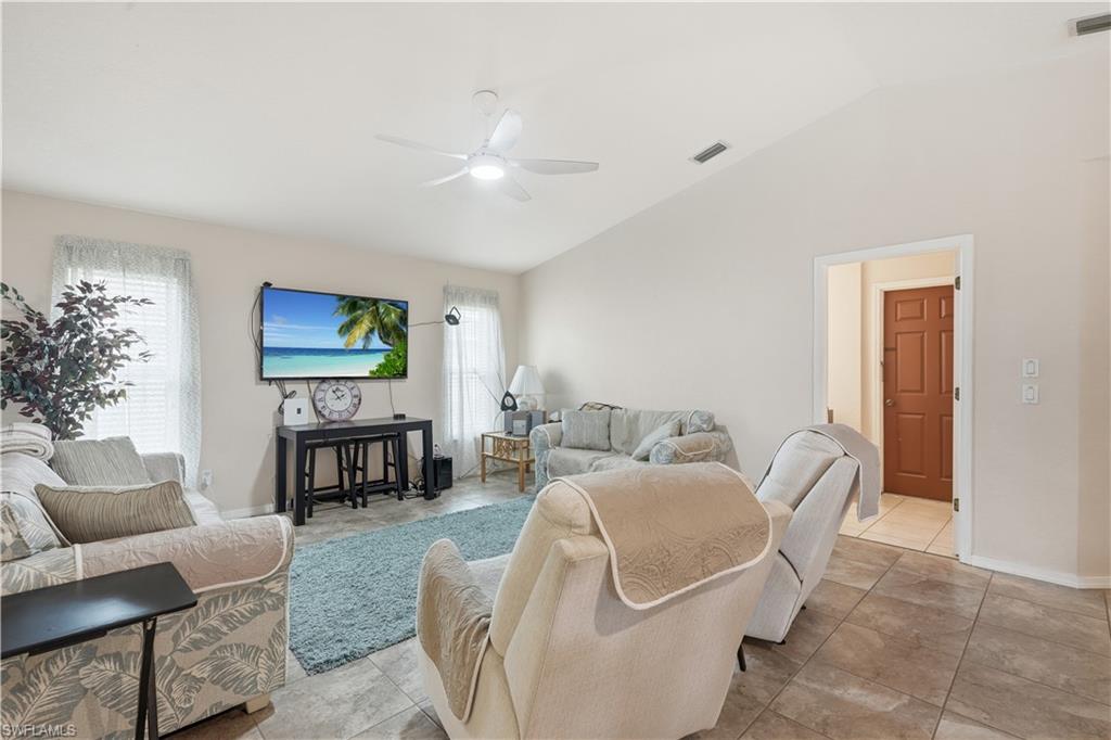 Living area featuring vaulted ceilings, tile flooring, a ceiling fan with integrated lighting, and multiple windows with blinds