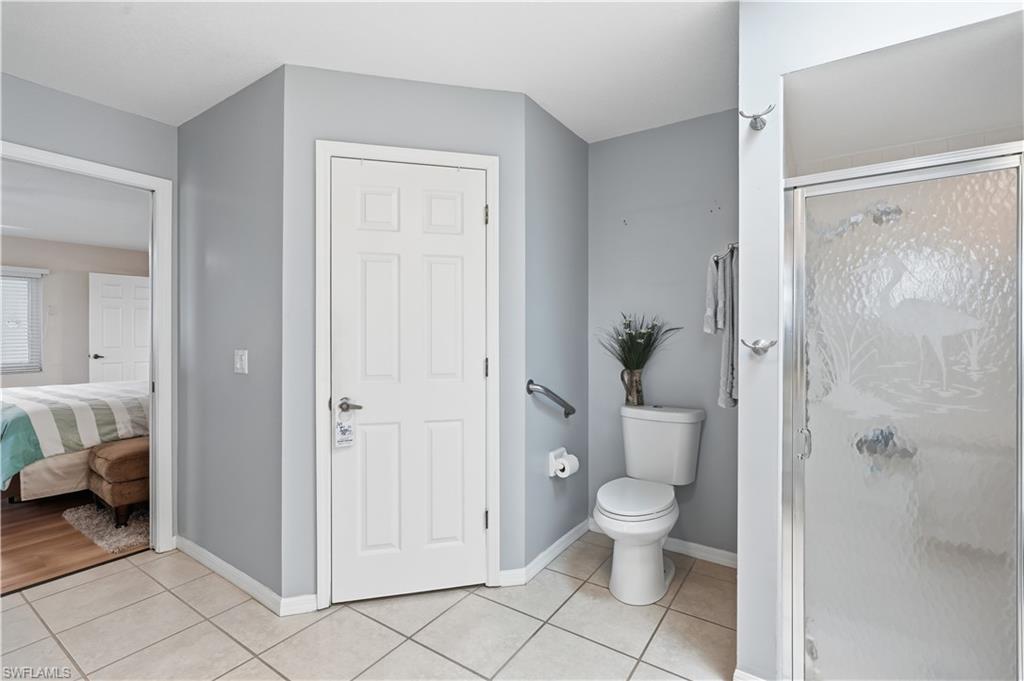Bathroom featuring a standing shower with frosted glass enclosure, white toilet, and light-toned tile flooring