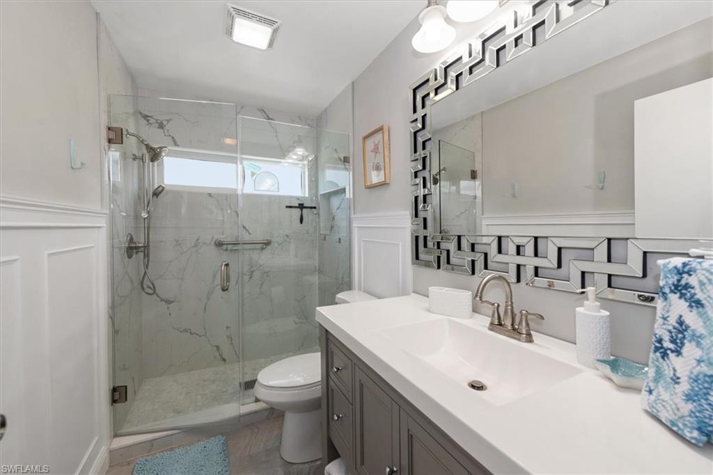 Full bathroom with a marble finish shower, vanity, a decorative wall, and a wainscoted wall