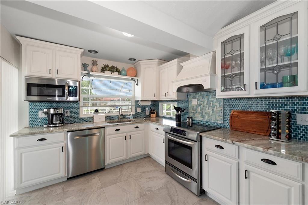 Kitchen featuring appliances with stainless steel finishes, custom range hood, white cabinetry, glass insert cabinets, and backsplash