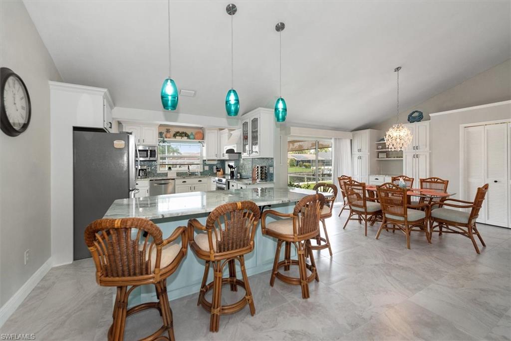 Kitchen featuring lofted ceiling, appliances with stainless steel finishes, light stone counters, a chandelier, and white cabinetry