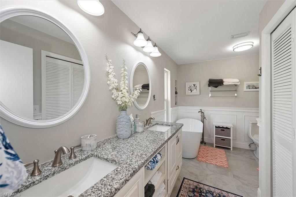 Full bathroom with a closet, double vanity, a wainscoted wall, a soaking tub, and a decorative wall