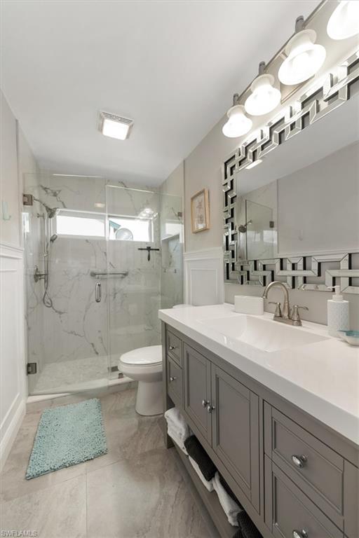 Full bath with a marble finish shower, vanity, a decorative wall, and a wainscoted wall
