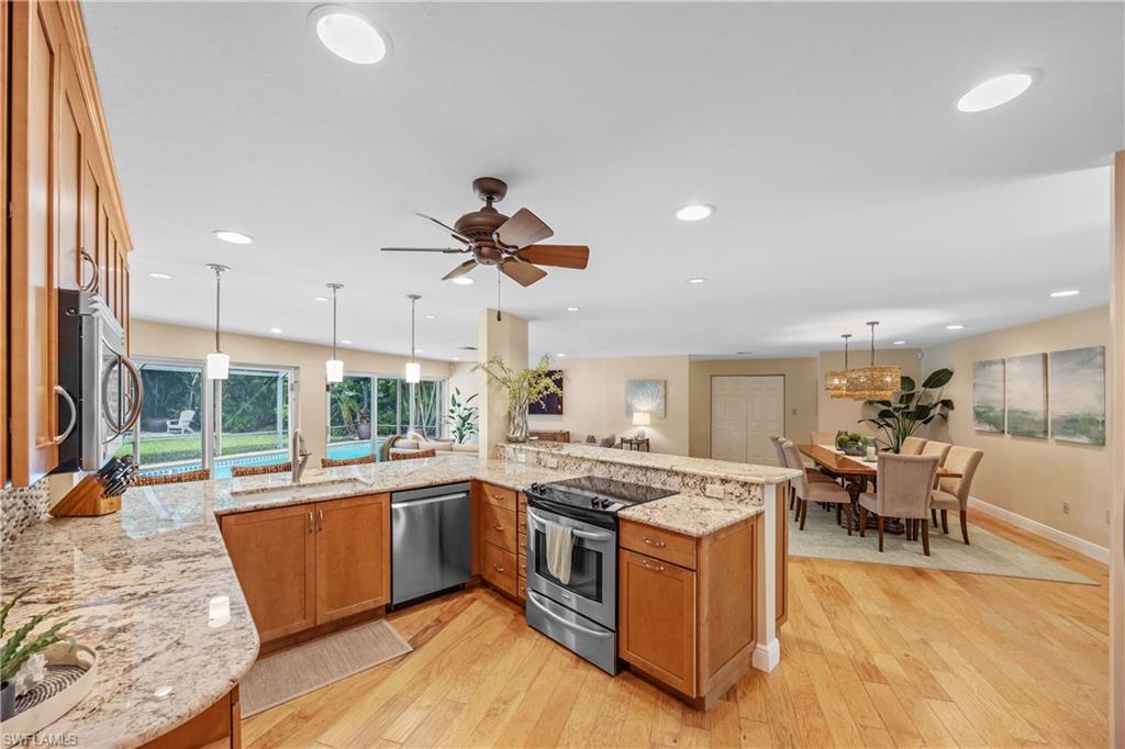 Kitchen with light hardwood / wood-style flooring, appliances with stainless steel finishes, hanging light fixtures, sink, and light stone counters