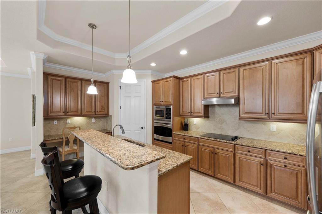 Kitchen with stainless steel appliances, hanging light fixtures, a tray ceiling, crown molding, and a breakfast bar area