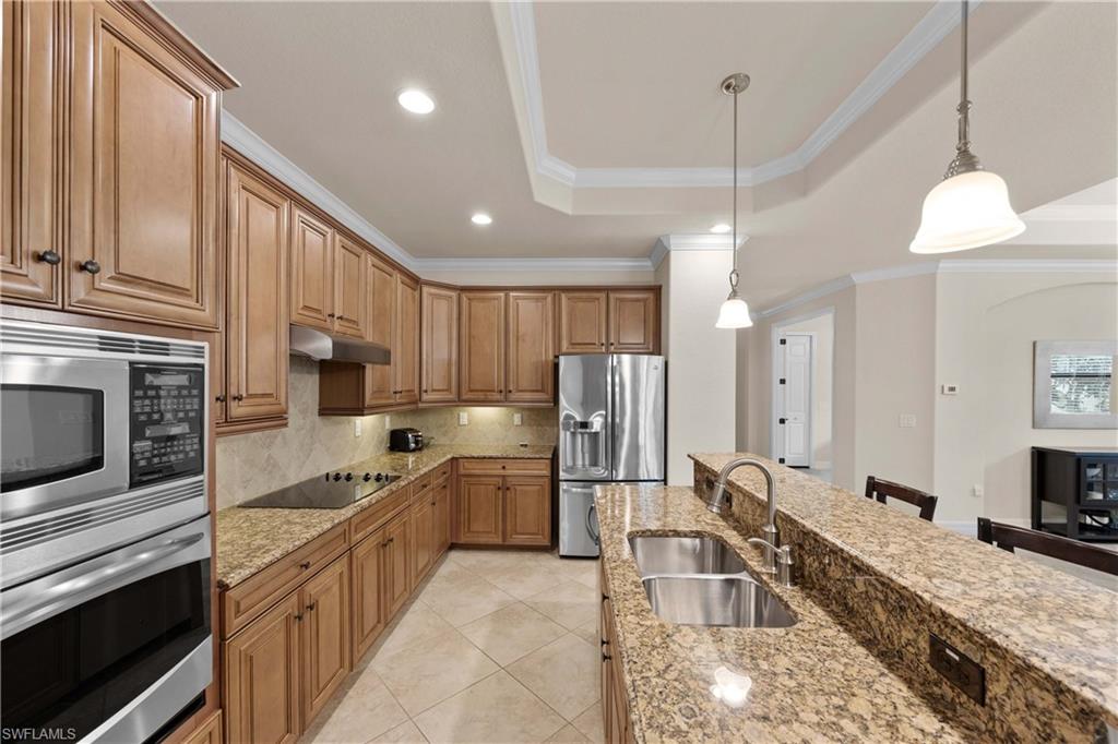 Kitchen with stainless steel appliances, a raised ceiling, light stone counters, hanging light fixtures, and sink