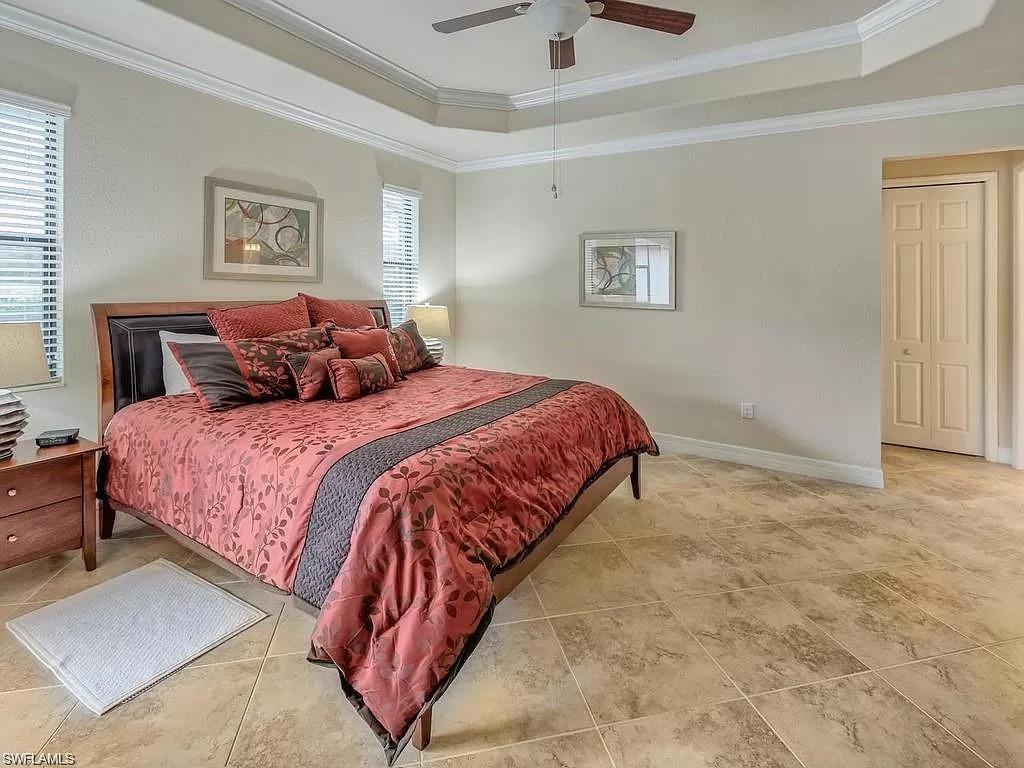 Bedroom with ceiling fan, crown molding, a tray ceiling, and light tile patterned floors