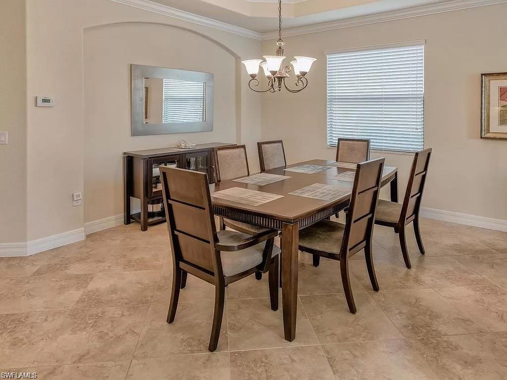 Dining area featuring light tile patterned flooring, a notable chandelier, ornamental molding, and a tray ceiling