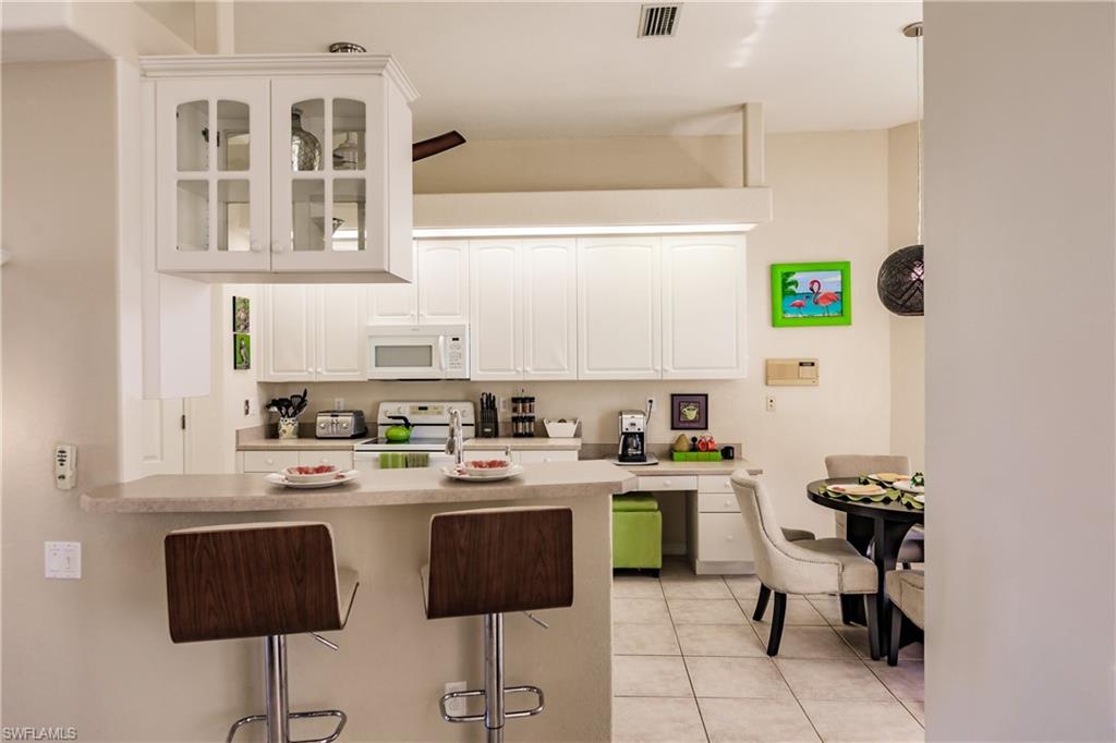 Kitchen with a breakfast bar, white appliances, lofted ceiling, white cabinets, and light tile patterned flooring
