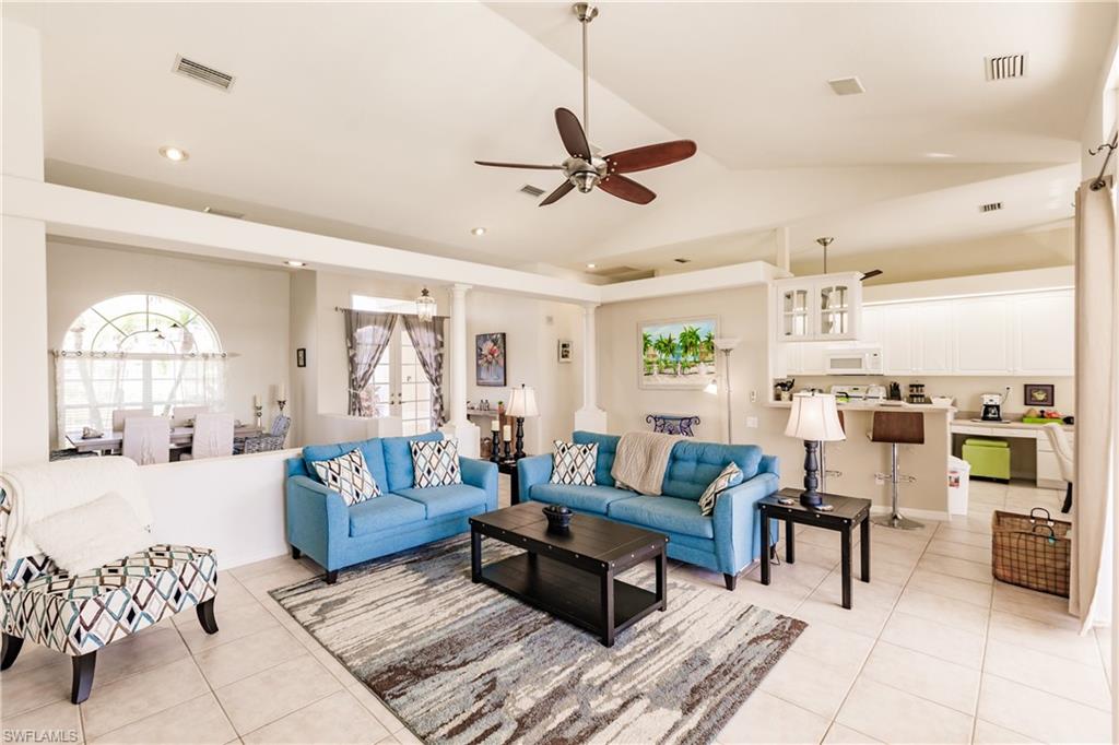 Living room featuring ceiling fan, light tile patterned flooring, ornate columns, and vaulted ceiling