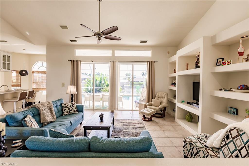 Tiled living room featuring built in shelves, ceiling fan, and lofted ceiling