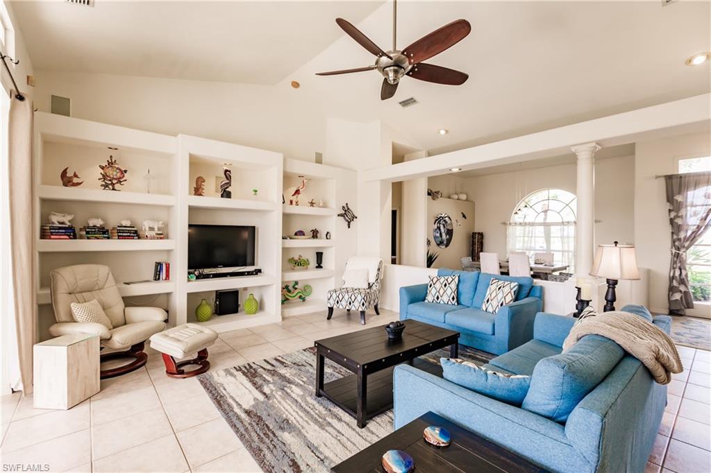 Tiled living room featuring built in shelves, decorative columns, vaulted ceiling, and ceiling fan