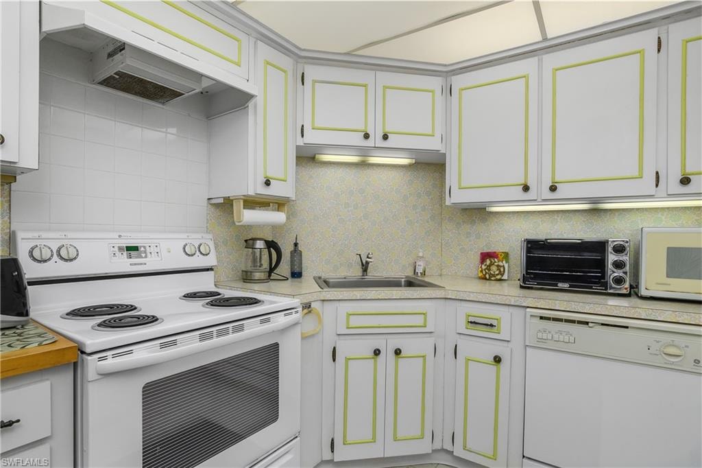 Kitchen with white appliances, premium range hood, light countertops, decorative backsplash, and white cabinetry