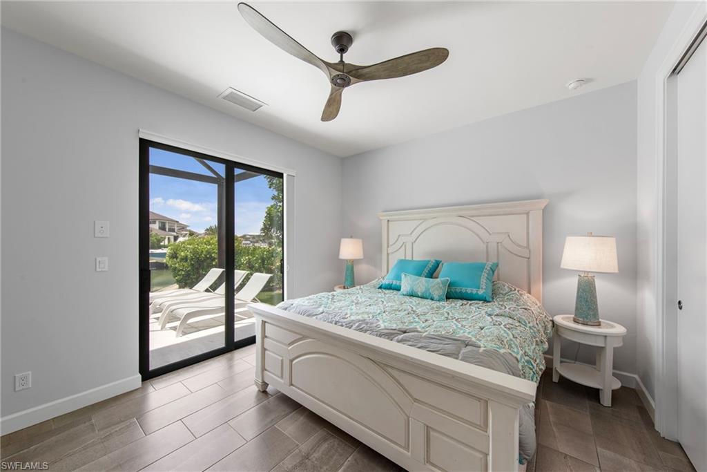 Sliding glass doors opening to an outdoor patio with lounge chairs, complemented by wood-finish flooring, a ceiling fan, and a built-in closet