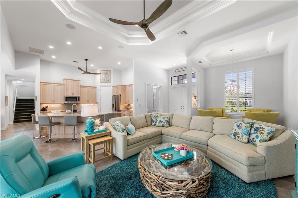 Open concept living area featuring tray ceilings with crown molding, recessed lighting, ceiling fans, and large windows with plantation shutters