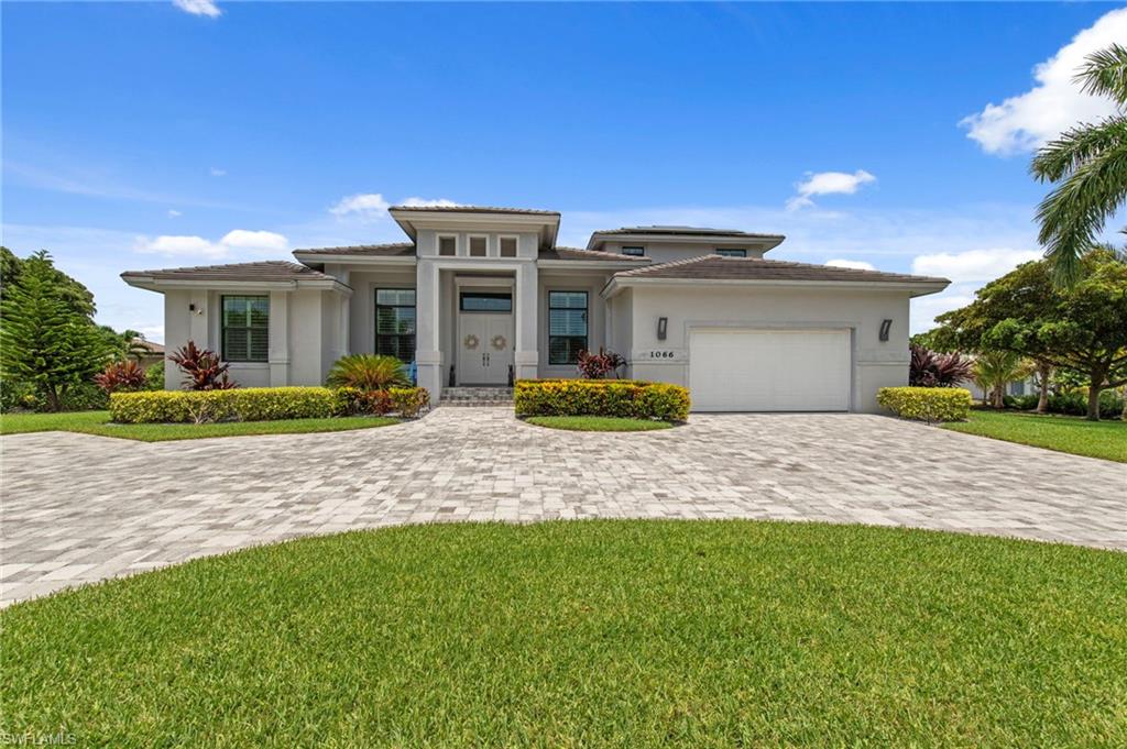 Contemporary exterior with a prominent portico entry, a paver driveway, an integrated garage, and manicured landscaping
