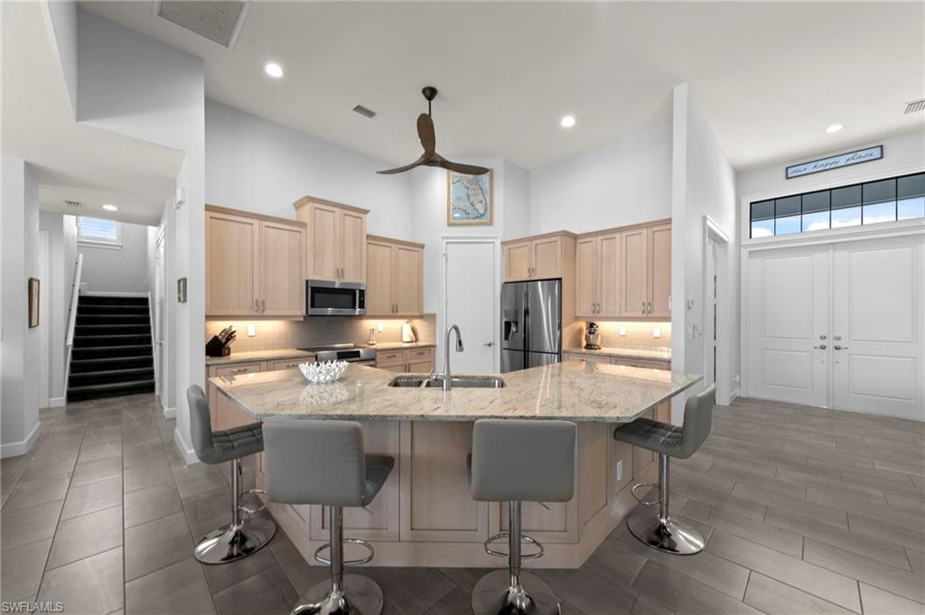 Open-concept kitchen featuring an angled island with seating, recessed lighting, wood cabinetry, and stainless steel appliances