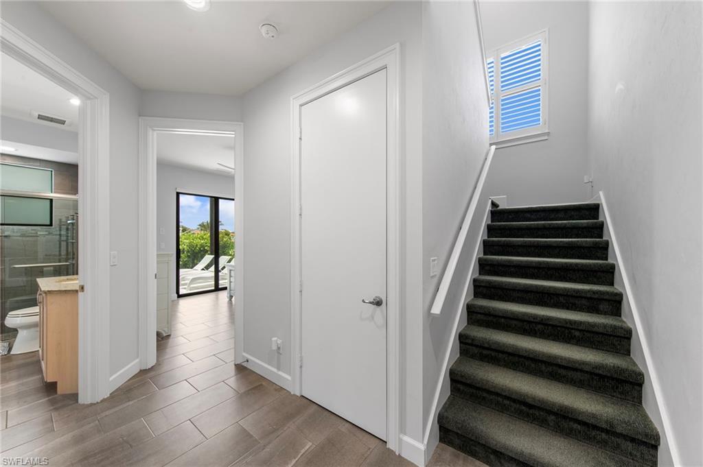 Staircase with dark carpeted treads and white handrail, featuring an upper window with louvered shutters