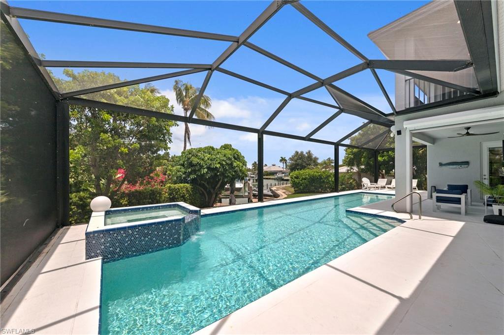 Screen-enclosed pool area featuring a rectangular swimming pool, integrated spa with blue mosaic tile, and concrete decking