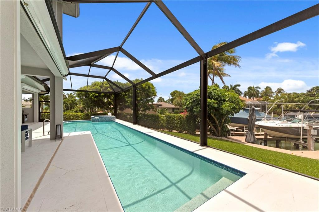 Screened-in outdoor living space with an elongated swimming pool, integrated spa, and direct water access