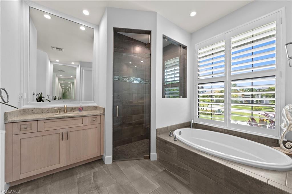 Soaking tub with a tiled surround, plantation shutters, and glass-enclosed shower with decorative tile inlay