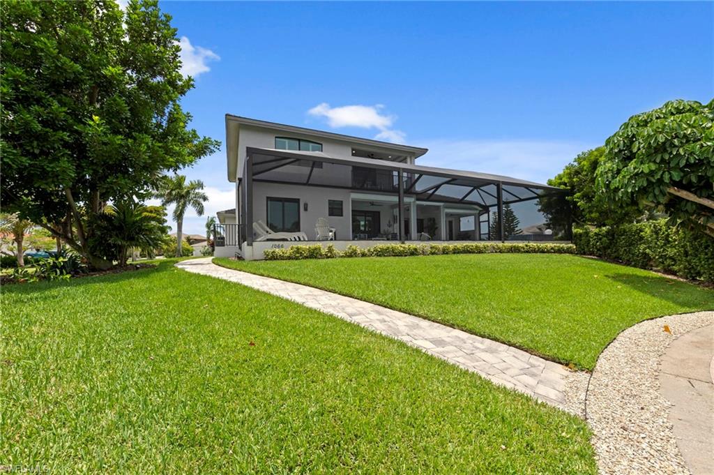 Contemporary two-story residence featuring a screened-in patio, expansive lawn, mature landscaping, and a paver pathway