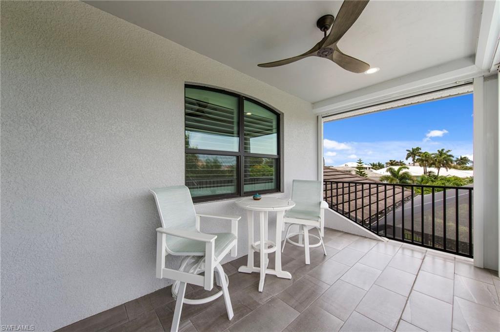 Covered outdoor balcony featuring tile flooring, textured exterior wall, arched window with horizontal blinds, and a ceiling fan with integrated lighting