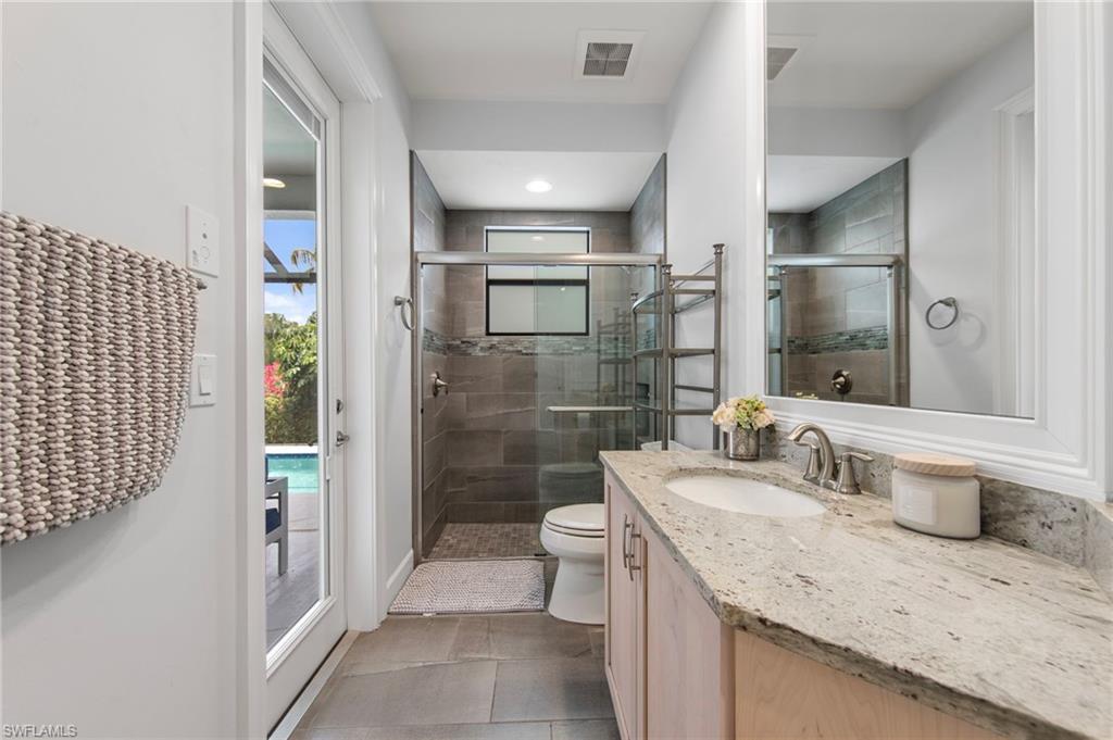 Bathroom featuring a single vanity with a light-toned countertop, a frameless shower with a glass enclosure, and a frosted glass door leading to an outdoor area with a pool